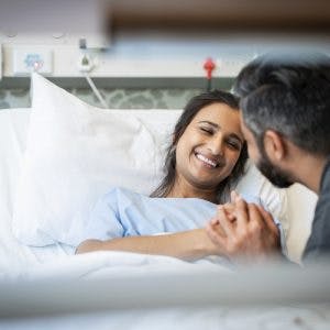 woman in hospital bed recovering from global anoxic brain injury and smiling at caregiver beside her