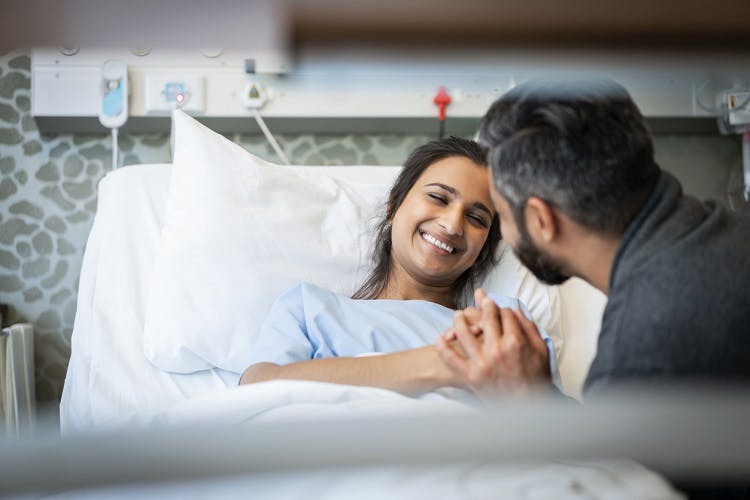 woman in hospital bed recovering from global anoxic brain injury and smiling at caregiver beside her