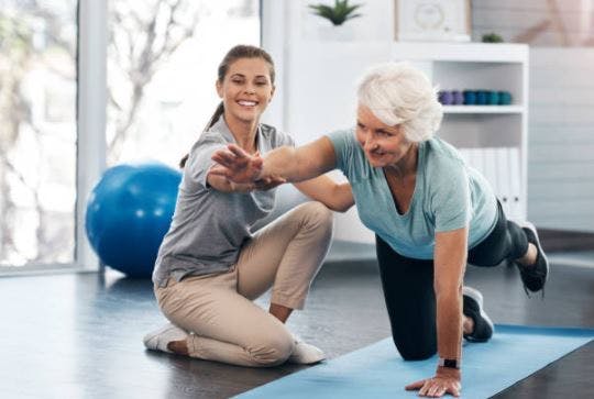 Physiotherapeut hilft älteren Schlaganfall-Überlebenden mit aktiver Bewegung aus einer vierfüßigen Position
