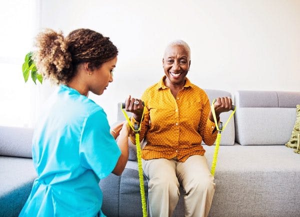 at-home therapist helps patient use physical therapy tools from the sofa