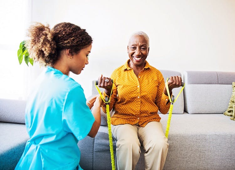 at-home therapist helps patient use physical therapy tools from the sofa