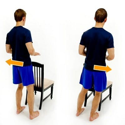 man demonstrating tbi exercise while holding onto the back of a chair for stability