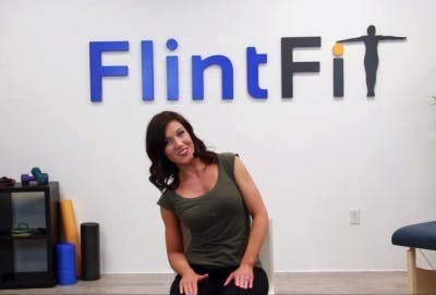 physical therapist seated in chair and leaning to left for oblique crunch core TBI exercise