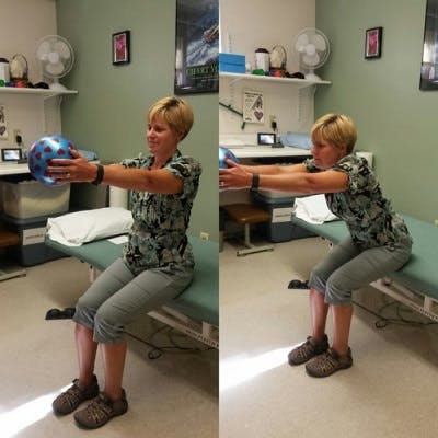 woman holding an exercise ball out in front of her while leaning forward