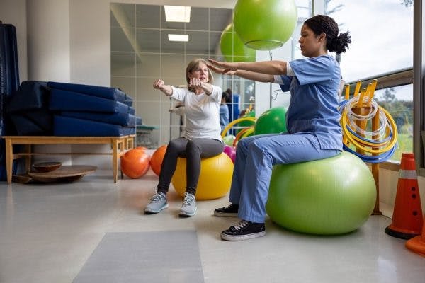 occupational therapist sitting on exercise ball showing a stroke patient an occupational therapy stroke intervention