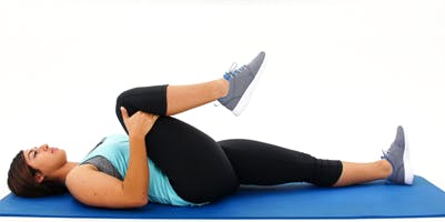 woman on mat holding right leg into chest for gait training exercise